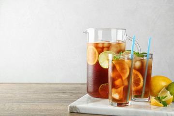Glasses and jug of refreshing iced tea on wooden table against light background. Space for text