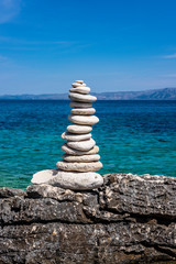 Fototapeta na wymiar Pebble tower standing on the beach in Proizd Island near Korcula Island, Dalmatia, Croatia, blue sky and clear Adriatic sea water, nice background image
