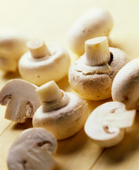 Whole and cut button mushrooms against a light wood background