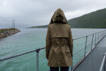 Blond hair woman walking along the pier enjoying scenic views. Ocean and rocks landscape. Lonely girl. Travel, adventure. Sense of freedom, lifestyle. Explore North Norway. Summer in Scandinavia