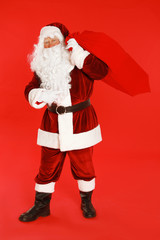 Authentic Santa Claus with bag full of gifts on red background
