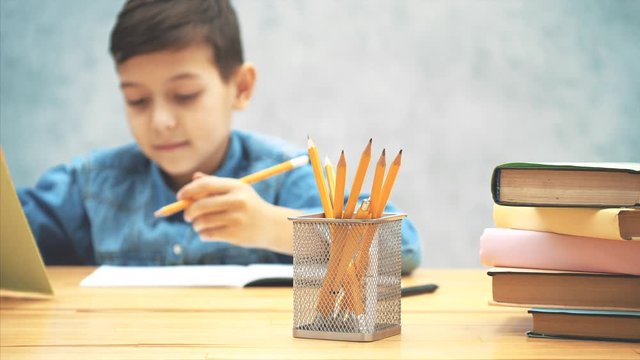 Blurred schoolboy is reaching pencil from the basket on the forefront, underlining something with ruler.