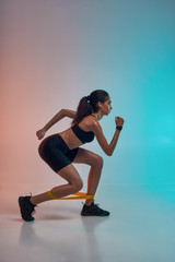 Fototapeta na wymiar I love fitness. Full length of young athlete woman in sports clothing exercising with a resistance band while standing in studio against colorful background
