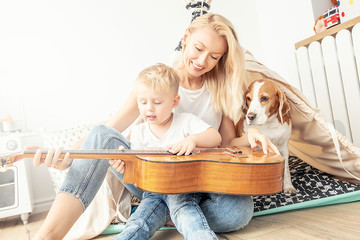 Little boy playing on guitar with mom .