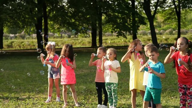 Happy little kids blowing soap bubbles in summer park