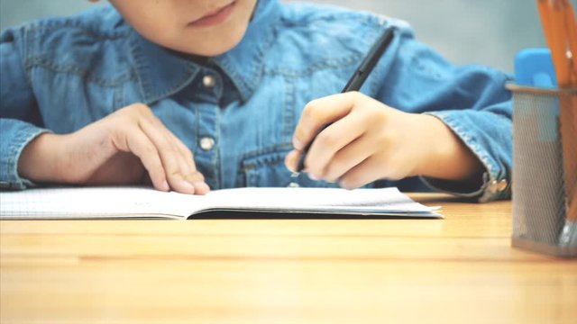Cropped hands of young concentrated school kid in blue jeans t-shirt writing, then highlighting the most important things in the copybook.