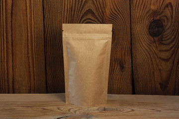 Brown kraft paper pouch bags with coffee beans front view on a wooden background.