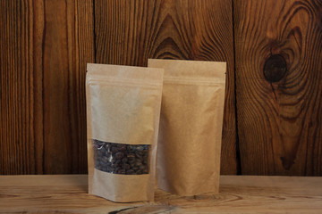 Brown kraft paper pouch bags with coffee beans front view on a wooden background.