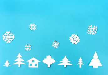 White paper figures of houses, Christmas trees and snowflakes on blue background