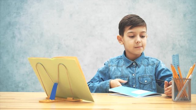 Young clever school kid in blue jeans t-shirt was writing, finished his homework, closed the copybook and now satisfied with the result.