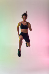 Fototapeta na wymiar Do it Full length of young athlete woman with perfect body in sports clothing jumping in studio against colorful background