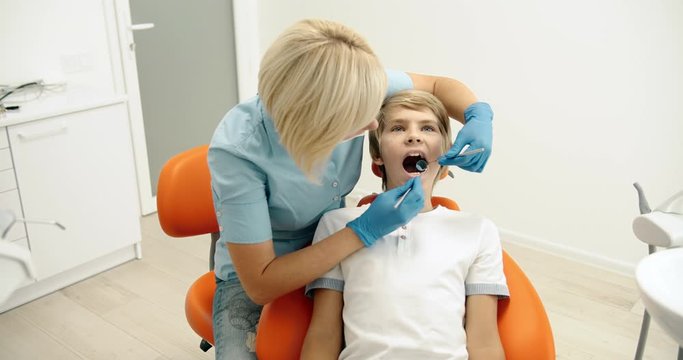 Experienced lady dentist checking preteen boy's jaw cavity, caries prevention, healthcare