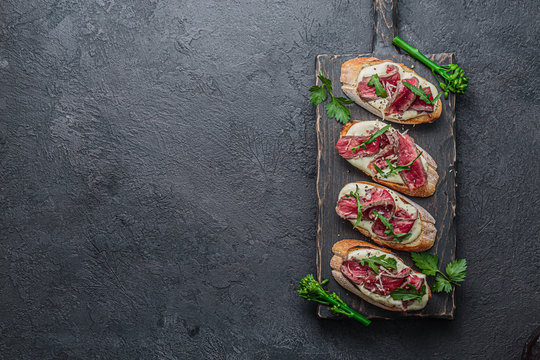 Crostini with roast beef on black board, copy space flat lay