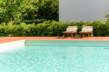 Sun loungers at a modern swimming pool in a green garden, relaxing in nature