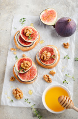 Bruschetta with fresh ricotta cheese, figs, nuts, thyme and honey on gray concrete background.