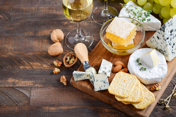 Cheese plate with grapes, crackers, honey, and nuts on a wooden table.
