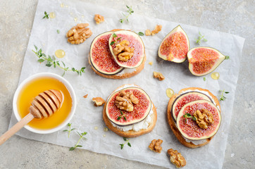 Bruschetta with fresh ricotta cheese, figs, nuts, thyme and honey on gray concrete background.