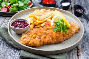 Deep fried Wiener schnitzel from veal topside with French fries and lettuce as closeup modern...