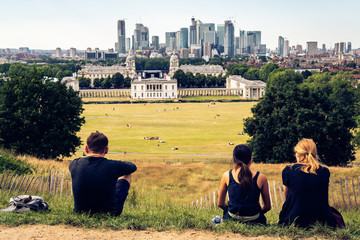 London panorama seen from Greenwich park viewpoint. Young people sitting in the foreground.