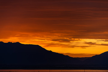 Sunrise with dark silhouette of mountains and orange red sunlight on Great Salt Lake in Antelope Island State Park from Ladyfinger campground in Utah