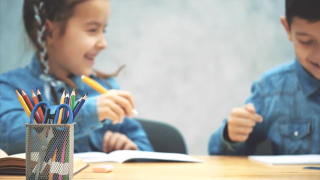 Blurred schoolkids, brother and sister, sitting at the table, writing, smiling.