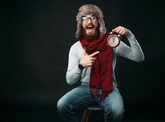 Portrait of amazed man with beard pointing at alarm clock