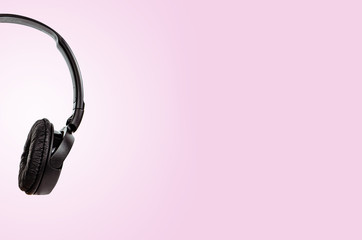 Black headphones on a pastel pink background. The concept of creating and listening to music. Comfortable headphones for listening to music. Creating sounds and listening to the foundations.