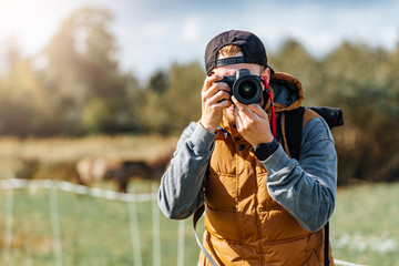 Photographer in brown vest and black hat taking pictures with his camera during sunny summer day. 