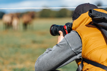 Photographer in brown vest and black hat taking pictures with his camera during sunny summer day. 