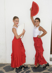Vertical portrait of two girls in a flamenco position. They are with flamenco fans and looking at the camera in a white background.