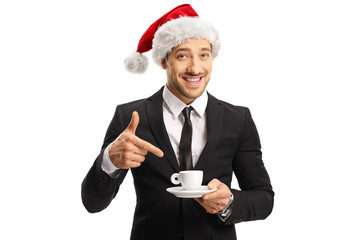 Man in a suit with a Santa hat holding a cup of coffee and pointing