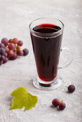 Glass of red grape juice on a gray concrete background. Side view