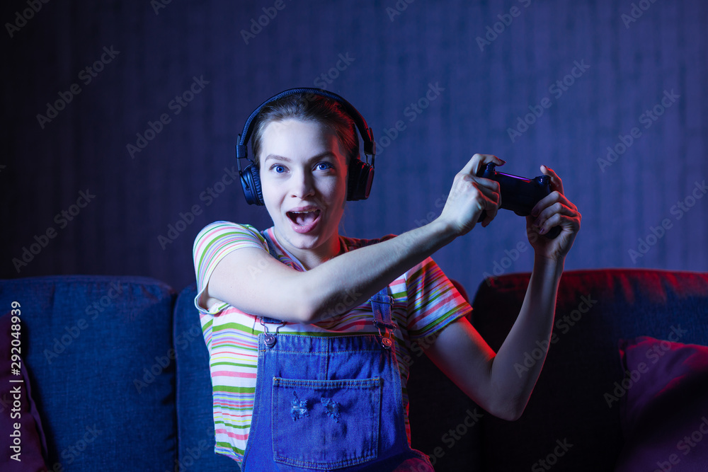 Wall mural a young girl plays games with the help of a joystick, gamepad.