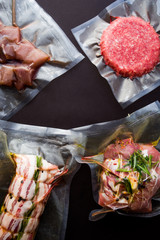 Sous vide raw pork and beef roast with hamburger and tuna ready to be cooked with a rooner, top view, flatlay on a dark background