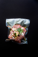 Sous vide cured pork neck ready to be cooked with a rooner, top view, flatlay on a dark background