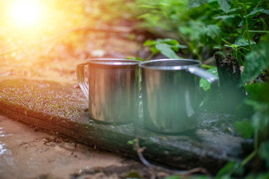 Two metal mugs stand on a shelf across a stream in the forest close-up. Photo with illumination, light © yaroslav1986