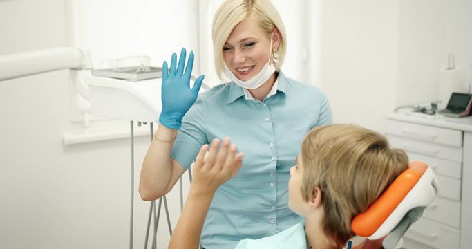Friendly smiling female dentist giving teenage boy high-five after successful procedure, oral cavity checkup