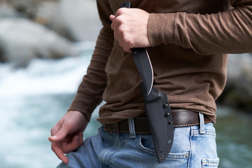 Man holding a tactical survival knife in the ready position outdoors in the wilderness.