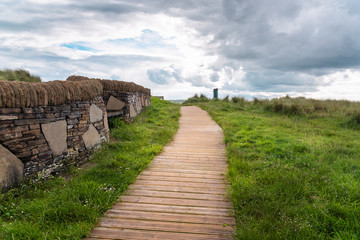 Fototapeta premium Empty boardwalk lined with a stone wall in a seaside park on a cloudy spring day