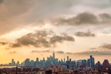 Cityscape of the New York City Skyline that includes Brooklyn and Manhattan under a cloud filled sky in the evening.
