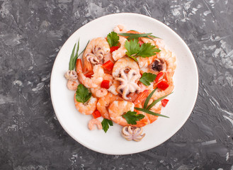 Boiled shrimps or prawns and small octopuses with herbs on white ceramic plate on a black concrete background. Top view.