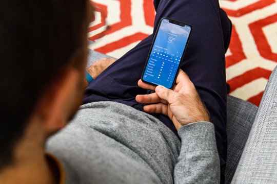 LONDON, UK - SEP 21, 2018: Man using the new Apple iPhone Xs with the immense OLED retina display and a12 bionic chip, looking over the app application weather app meteo in Paris France