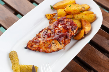 Bbq grilled chicken breast with baked jacket potatoes and pickled cucumbers on a summer terrace