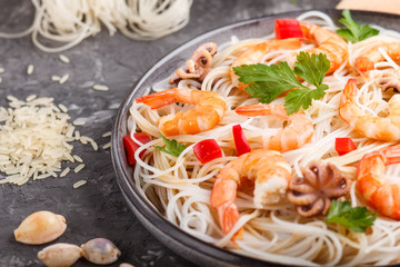 Rice noodles with shrimps or prawns and small octopuses on gray ceramic plate on a black concrete background. side view, close up.