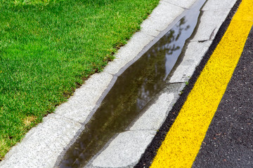 flowing rainwater in the filled canal is a cement ditch of a drainage system on the side of wet tarmac road after rain.