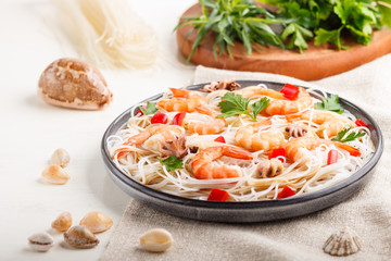 Rice noodles with shrimps or prawns and small octopuses on gray ceramic plate on a white wooden background. side view, selective focus.