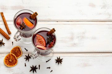 Hot red mulled wine or gluhwein in glass with orange, cinnamon sticks and anise on white wooden background.