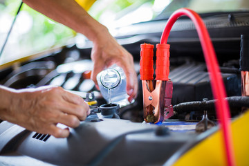 Hands of mechanic check water in yellow car radiator and add water to car radiator with charging car battery with electricity trough cables. Service and maintenance vehicles, Selective focus.