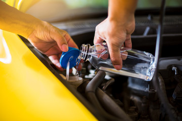 Mechanic fill fresh water into windscreen or in water tank wiper on yellow car  engine room. Service and maintenance of yellow cars or vehicles.