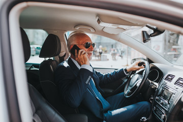 Senior good looking businessman talking on mobile phone while driving his car .